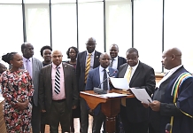 Hon. Major General (Rtd) Kahinda Otafiire taking Oath of Allegiance as an Ex-Officio Member of the Assembly flanked by several Members.