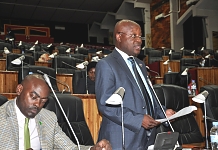 Hon Mike Sebalu presents the report of the Committee to the House as Hon Mukasa Mbidde pays attention to the proceedings